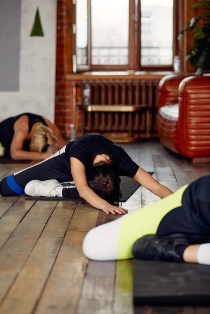 Foto pequeño grupo de personas con hábitos saludables haciendo ejercicios de estiramiento en el piso del gimnasio enfoque selectivo en la mujer morena