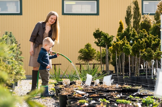 El pequeño hijo ayuda a mamá a regar las macetas de plantas en el centro de jardinería