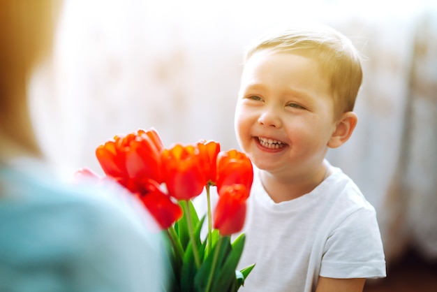 El pequeño hijo felicita a la madre y le da un ramo de tulipanes de flores. Feliz día de la madre.