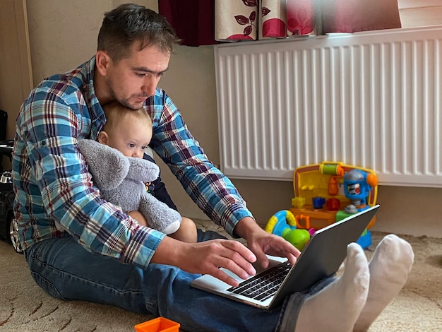 El pequeño hijo con su papá está sentado en la computadora portátil en la habitación