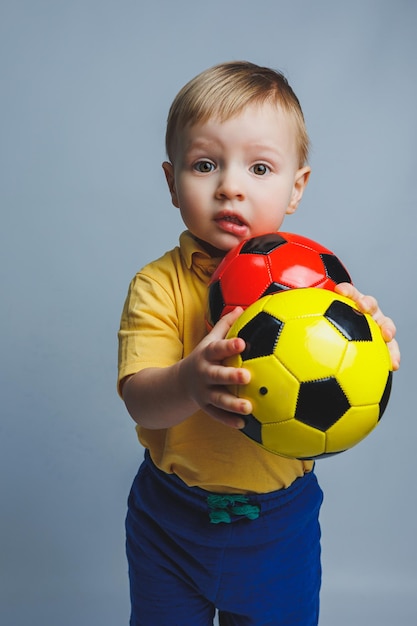 Foto un pequeño hincha o jugador europeo con uniforme amarillo y azul con un balón de fútbol apoya al equipo de fútbol sobre un fondo blanco concepto de estilo de vida del juego deportivo de fútbol aislado sobre fondo blanco