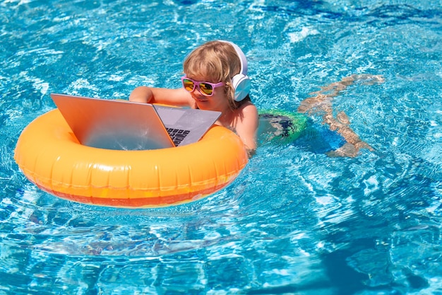 Pequeño hombre de negocios independiente en viajes de verano niño trabajando a distancia en una computadora portátil en la piscina