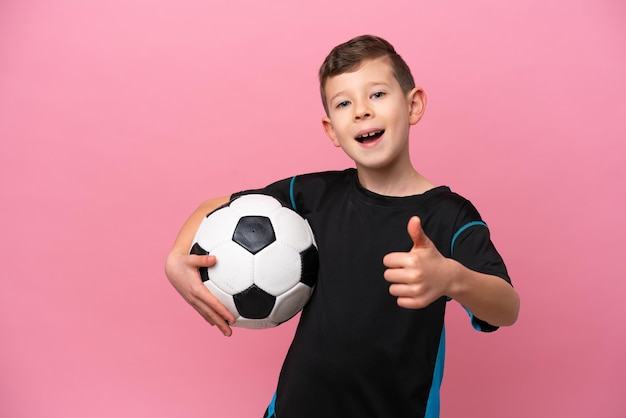 Un pequeño jugador de fútbol caucásico aislado en un fondo rosado con los pulgares hacia arriba porque algo bueno sucedió