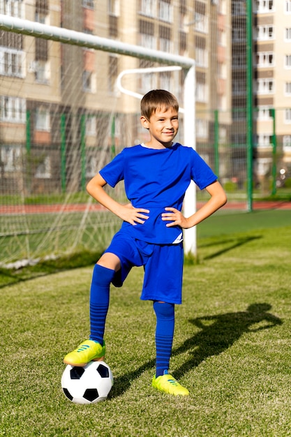 Un pequeño jugador de fútbol con una pelota se encuentra en un campo de fútbol verde en la portería.