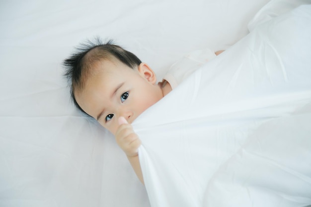 Pequeño y lindo bebé asiático en la cama con una manta suave en el interior