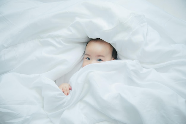 Pequeño y lindo bebé asiático en la cama con una manta suave en el interior