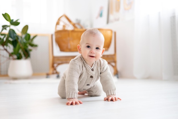 Pequeño y lindo bebé con un traje tejido de lana pastel aprendiendo a gatear en el suelo en una luminosa sala de estar bebé sonriendo jugando al desarrollo temprano de los niños