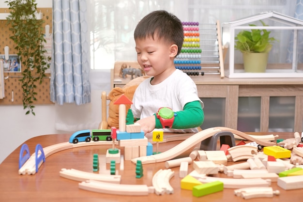 Pequeño y lindo niño asiático de 5 años divirtiéndose jugando con tren de madera