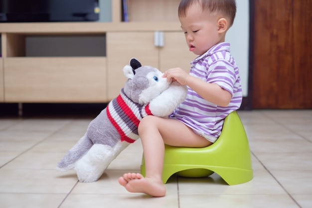 Pequeño y lindo niño asiático bebé niño sentado en el orinal jugando con su perro de peluche de juguete