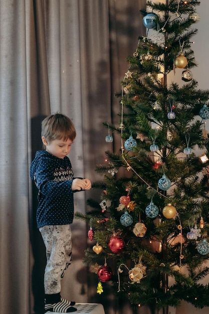 Pequeño y lindo niño caucásico decorando el árbol de Navidad con adornos centelleantes