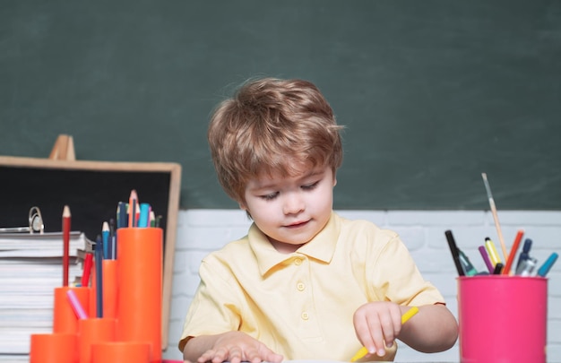 Un pequeño y lindo niño preescolar estudia en un salón de clases. Niño sonriente alegre Alumno divirtiéndose contra la pizarra. Niño sonriente alegre en la pizarra.