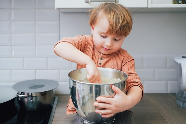 Pequeño y lindo niño preescolar rubio horneando pasteles en la cocina doméstica en el interior