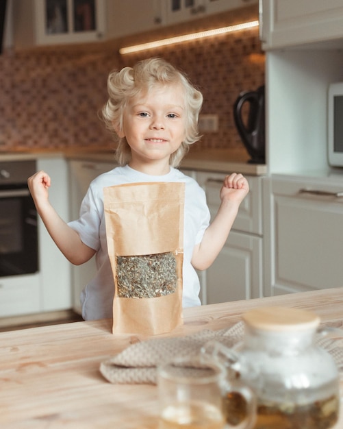 Un pequeño y lindo niño sonriente muestra su alegría y deseo de beber té de hojas reales