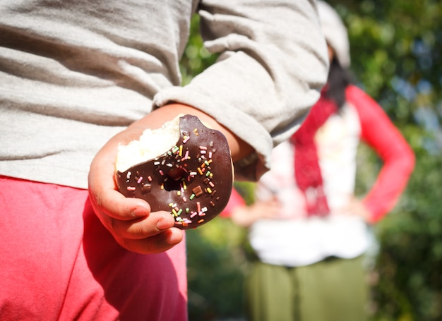 pequeno menino escondendo uma rosquinha de chocolate atrás das costas