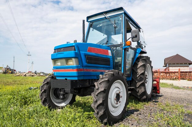 Foto un pequeño mini tractor azul se encuentra en un patio de granja sobre hierba verde y espera a que comience el trabajo