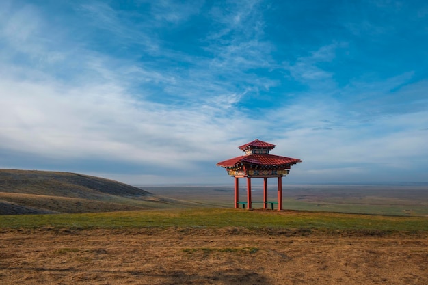 Un pequeño mirador en medio de un campo con cielo azul y nubes.