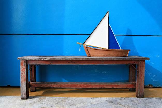 Pequeño modelo de juguete de barco de madera en una silla larga de madera con fondo de hormigón azul