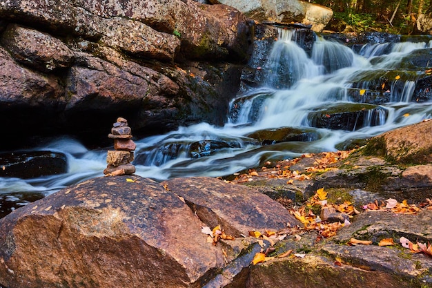 Pequeno monte de pedras em rochas cobertas de folhas ao longo de cachoeiras em cascata