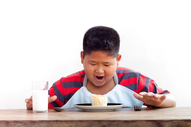 El pequeño muchacho asiático disfruta de su torta de la taza en el fondo blanco.