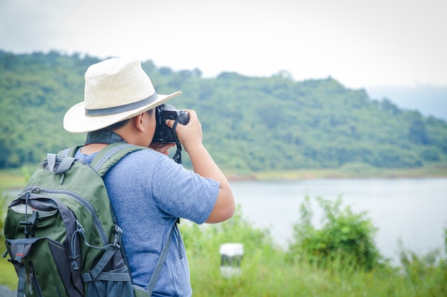 A un pequeño muchacho asiático con sombrero le gusta viajar a la naturaleza. Sostenga la cámara para tomar una foto de paisaje