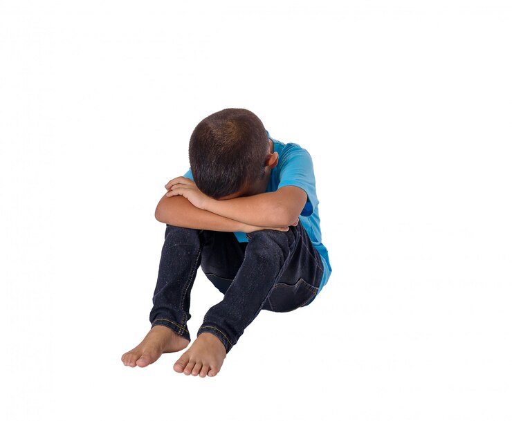 Pequeño muchacho asiático triste que se sienta en el piso aislado en blanco