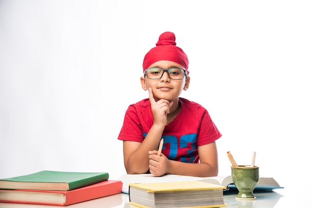 Pequeño muchacho indio sij estudiando en la mesa de estudio con libros