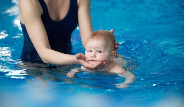 Pequeño nadador infantil Vista recortada de la madre entrenando a su bebé recién nacido flotando en la piscina Bebé buceando en el agua