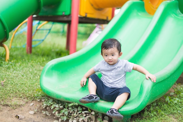 Pequeño niño asiático jugando tobogán en el patio de recreo