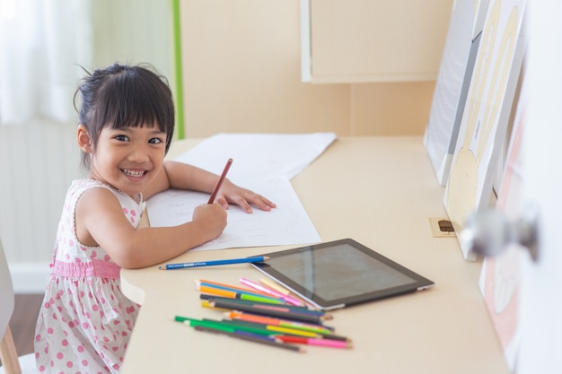 Pequeño niño asiático que usa un lápiz para escribir en el cuaderno en el escritorio