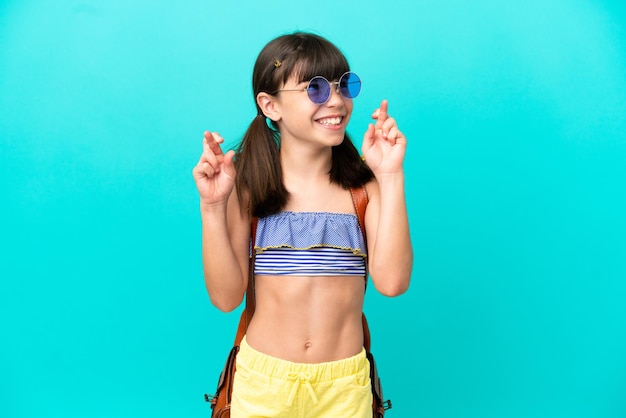 Pequeño niño caucásico yendo a la playa aislado de fondo azul con los dedos cruzados