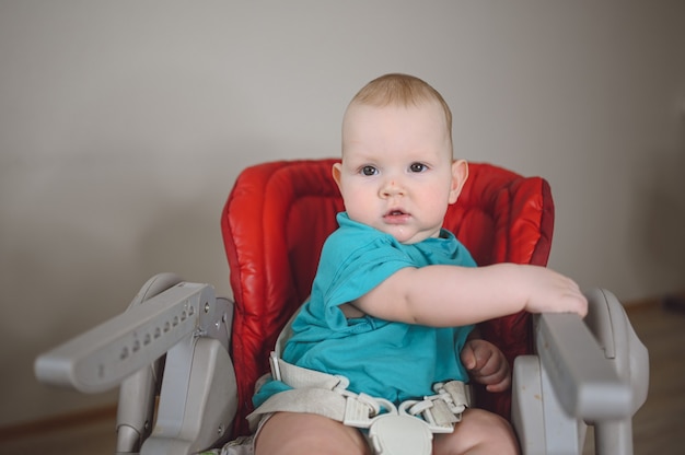 Pequeño niño divertido niño recién nacido emocional sentado en la alimentación de las expresiones faciales del bebé silla alta y