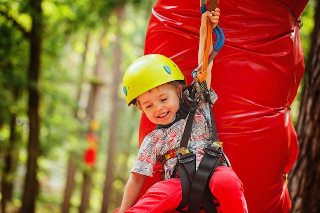 Pequeño niño feliz del niño en parque de la aventura en el equipo de seguridad en día de verano