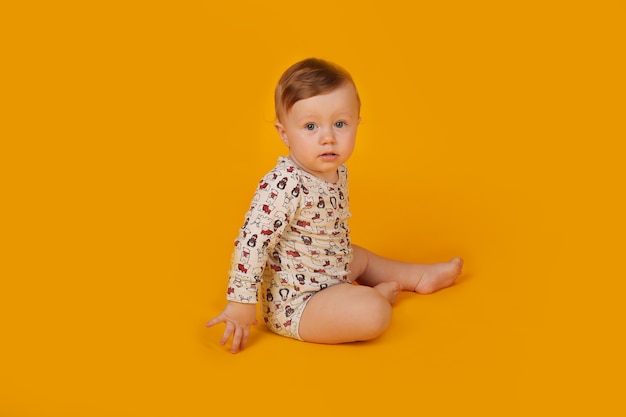 un pequeño niño hermoso con ojos azules en un traje está sentado sobre un fondo amarillo