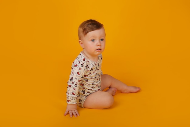 un pequeño niño hermoso con ojos azules en un traje está sentado sobre un fondo amarillo