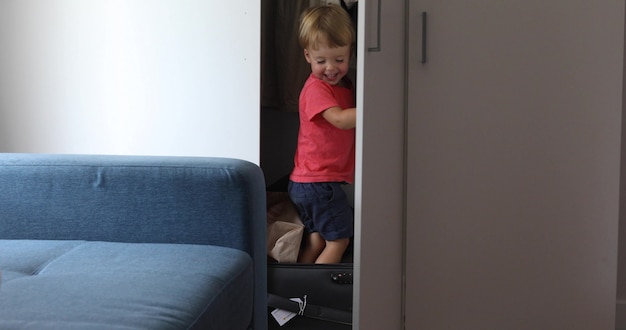 Pequeño niño jugando en casa un juego de viajero infantil en una maleta de viaje