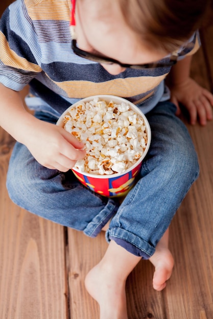 Pequeño niño lindo bebé 23 años 3d imax gafas de cine con cubo para palomitas de maíz comiendo comida rápida sobre fondo de madera Concepto de estilo de vida infantil para niños Copiar espacio