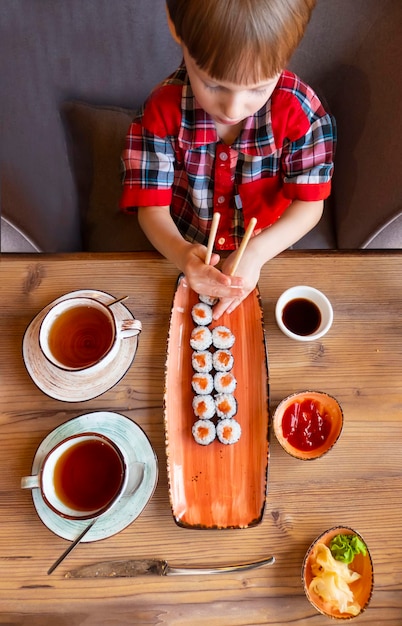 Pequeño niño lindo comiendo sushi en un café concepto de comer vista superior del niño comiendo sushi con palillos