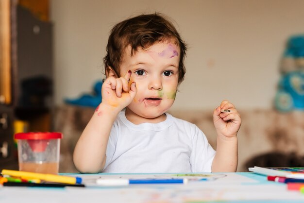 Un pequeño niño lindo dibuja con pinceles y pinturas de colores en una hoja de papel.