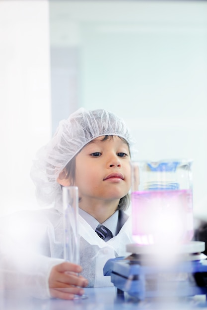 Pequeño niño lindo inteligente que experimenta con los tubos de ensayo en laboratorio moderno real del hospital
