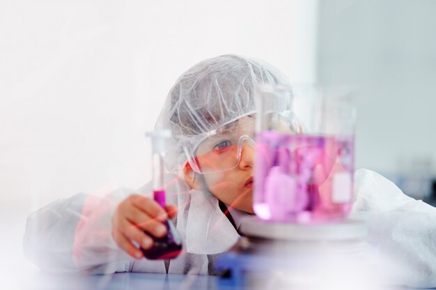 Pequeño niño lindo inteligente que experimenta con los tubos de ensayo en laboratorio moderno real del hospital