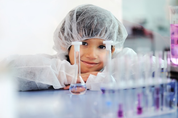 Pequeño niño lindo inteligente que experimenta con los tubos de ensayo en laboratorio moderno real del hospital