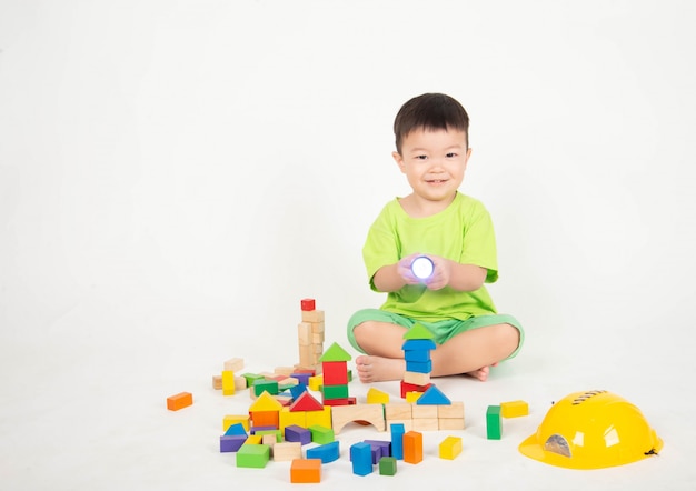 Pequeño niño pequeño asiático que juega los bloques de madera usan el ingeniero del casco