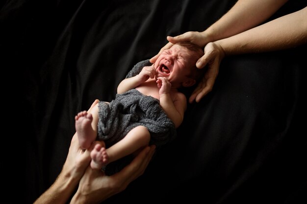 Pequeño niño recién nacido en negro. La parte superior e inferior del niño sostienen las manos de los padres.