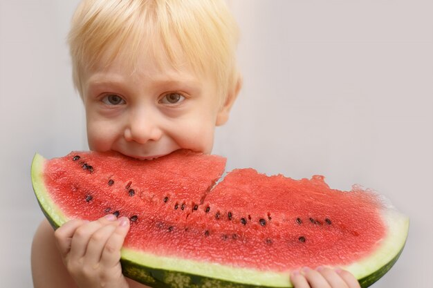 El pequeño niño rubio come un gran trozo de sandía.