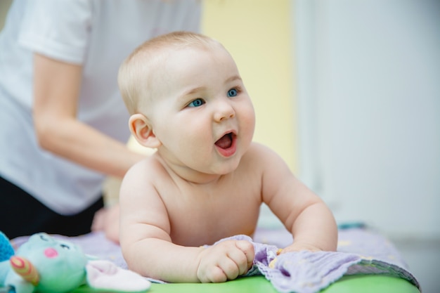 Un pequeño niño sonriente acostado boca abajo recibe un masaje en una sala de masajes que tiene un juguete en la boca