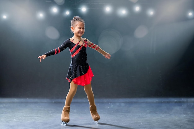 Pequeño patinador monta anillos en vestido rojo y negro en pista de hielo