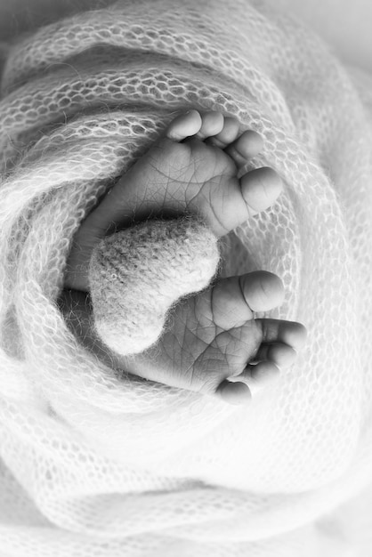 El pequeño pie de un bebé recién nacido Los pies suaves de un recién nacido en una manta de lana Un primer plano de los dedos de los pies, los talones y los pies de un recién nacido Un corazón tejido en las piernas de un bebé Fotografía macro en blanco y negro