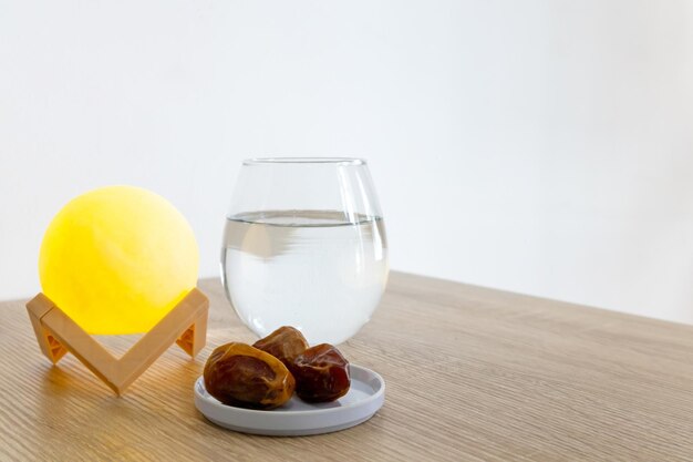 Un pequeño plato de dátiles en una mesa de madera con un vaso de agua y una lámpara