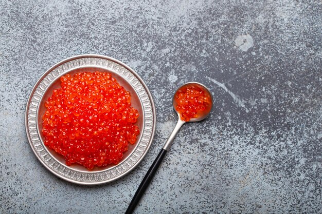 Foto pequeno prato de metal com caviar de salmão vermelho e uma colher de cima.