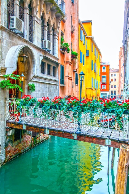 Pequeño puente con flores sobre un estrecho canal en Venecia, Italia